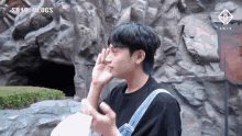 a man covering his face with his hand in front of a rock wall with sb19 ulogs written on it