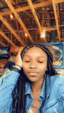 a woman in a denim jacket is sitting in a restaurant with her eyes closed and her hand on her head .