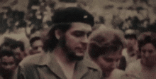 a man with a beard wearing a hat is standing in front of a crowd .