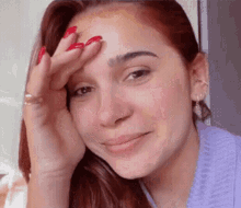 a woman with red nails and a nose ring holds her hand to her face