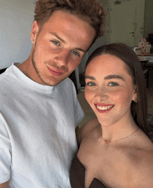 a man and a woman are posing for a picture and the man is wearing a white t-shirt