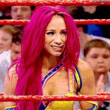 a woman with pink hair is standing in a wrestling ring .