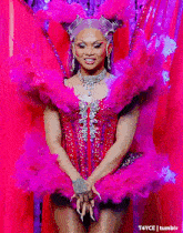 a drag queen is wearing a pink costume with feathers and a crown on her head .