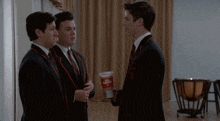 three men in suits and ties are standing next to each other and one of them is holding a can that says " ice cream "