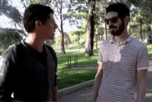two men are standing next to each other in a park and talking