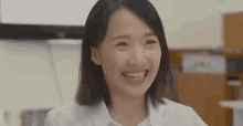 a young woman in a white shirt is smiling while sitting at a desk .