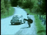 a man is carrying a guitar case down a road while a car is driving by .