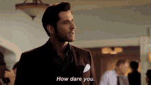 a man in a suit is standing in a room and saying `` how dare you . ''