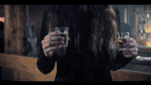 a woman in a black dress holds two shot glasses in her hands