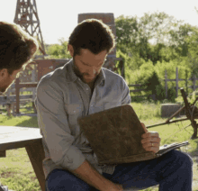 a man is sitting at a picnic table holding a book