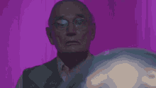 an elderly man wearing glasses is standing in front of a purple curtain .