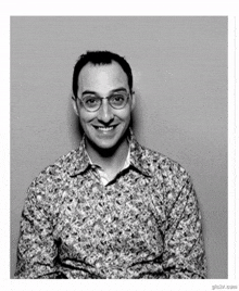 a man wearing glasses and a floral shirt is smiling