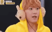 a man wearing a yellow hoodie and ear muffs is holding a stuffed animal .