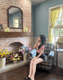a woman sits in a chair in front of a fireplace with flowers in front of it