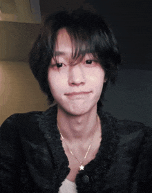 a young man wearing a black jacket and a gold necklace with a star pendant