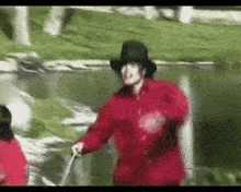 a man in a red jacket and black hat is walking across a grassy field