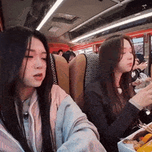 two girls are sitting on a bus and one of them is eating food