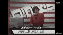 a woman in a red sweater is standing in front of a computer with hebrew writing on it .