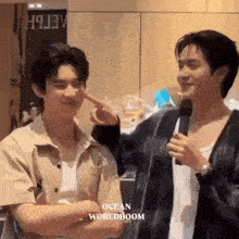 two young men are standing next to each other and one of them is holding a microphone and pointing at the other 's face .