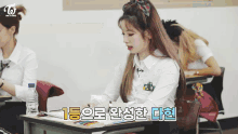 a girl sits at a desk in a classroom with a twice logo on the wall
