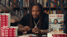 a man sits at a table with stacks of yeast mode books in front of him