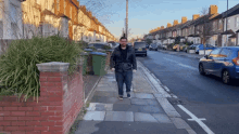 a man walks down a sidewalk in front of a row of houses and cars