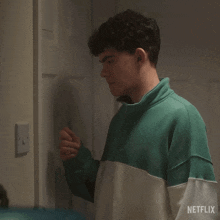 a young man in a green and white sweatshirt is standing next to a door .