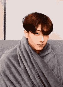 a young man is wrapped in a gray blanket and sitting on a couch .
