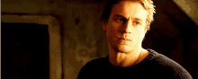 a man in a black sweater is looking at the camera with a serious look on his face