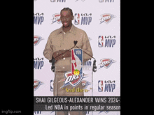 a man stands at a podium with a oklahoma city thunder logo on the wall behind him
