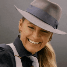 a woman wearing a fedora hat and suspenders smiles