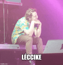 a man is sitting on a stage with a microphone in his hand and the word leccike written below him