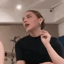 a woman wearing a black shirt and earrings is standing in a room with her mouth open .
