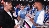 a man in a suit is holding a tray of donuts in front of a group of people wearing blue shirts that say sketch