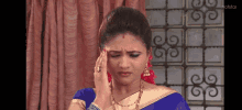 a woman in a blue and gold sari is holding her head