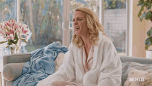 a woman is sitting on a couch with a blanket that says netflix on the bottom