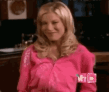 a woman in a pink jacket is sitting in a kitchen and smiling .