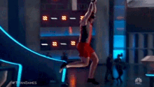 a man in a red shirt is falling from a building with the hashtag #titangames on the bottom