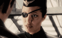 a woman wearing an eye patch and a hat looks at a man .