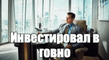 a man in a suit and tie is sitting at a desk in front of a window with a caption in russian .