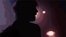 a man wearing a pearl necklace and a leather jacket is standing in front of a red light .