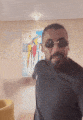 a man wearing sunglasses and a black shirt is dancing in front of a painting