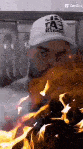 a man wearing a white hat is standing in front of a fire .
