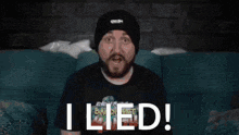 a man with a beard wearing a black beanie is sitting in a living room and says i lied .