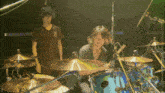 a man playing a drum set with the letter d on the bottom right