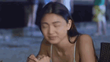a woman in a bikini top is sitting at a table with her eyes closed .