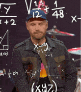 a man in a blue hat stands in front of a blackboard with mathematical equations drawn on it