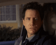a man in a blue jacket and tie is sitting in the back seat of a car