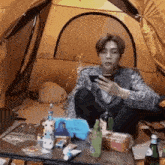 a man is sitting in a tent looking at a cell phone .