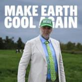 a man wearing a green make earth cool again hat stands in a grassy field
